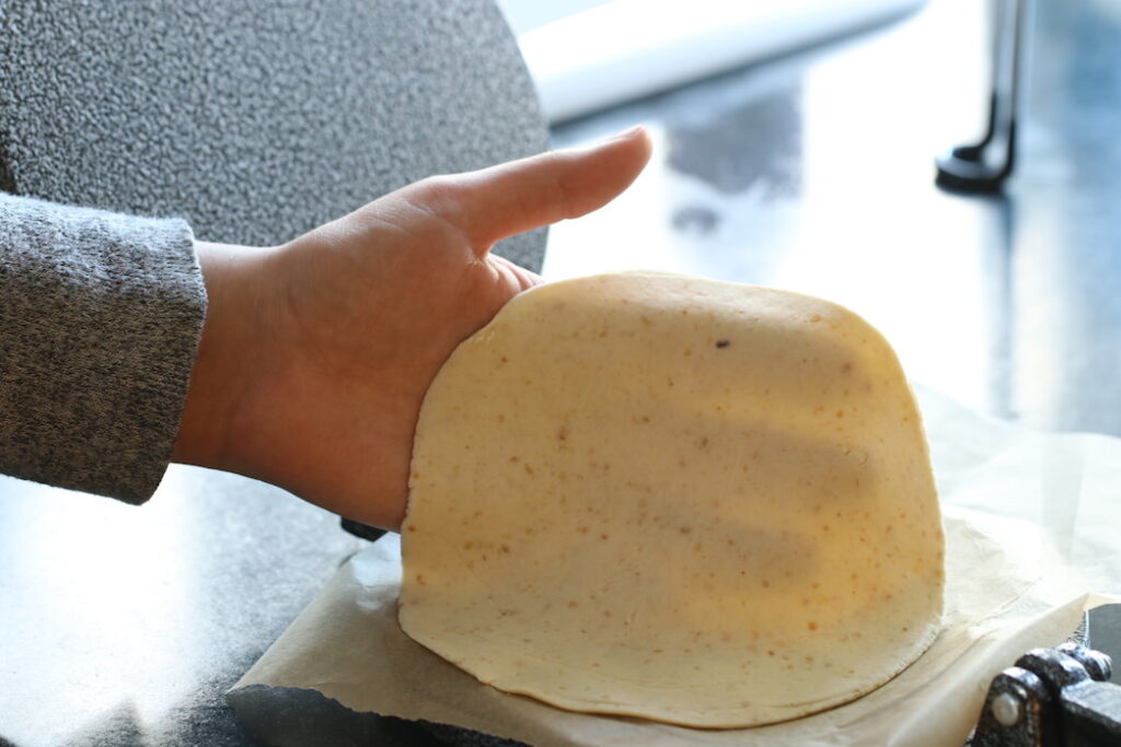 Girl's hand holding a tortilla that was just flattened using a cast iron tortilla press