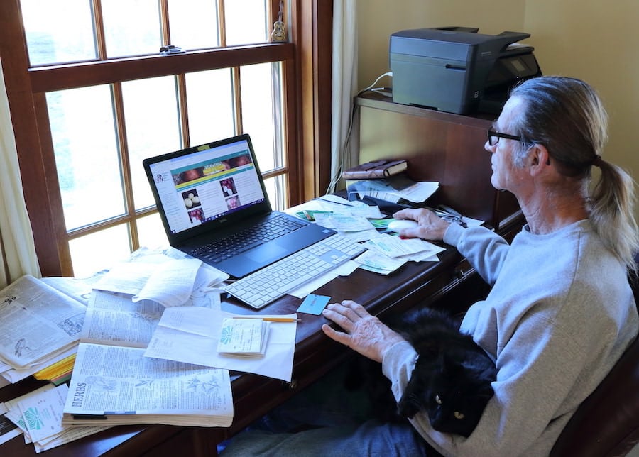 Jamie sitting at his desk with out cat on his lap, using his computer to order seeds