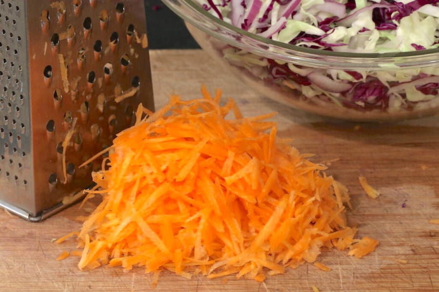 A bowl of shredded cabbages; a box grater with a mound of shredded carrots