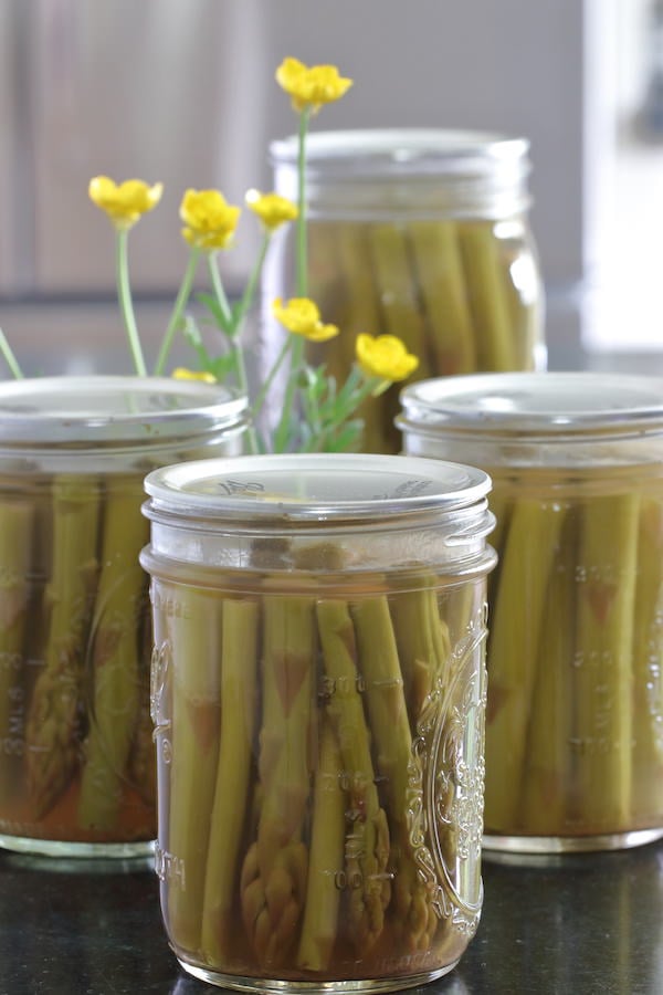 1 quart and 3 pint jars of canned pickled asparagus with a small arrangement of buttercup flowers