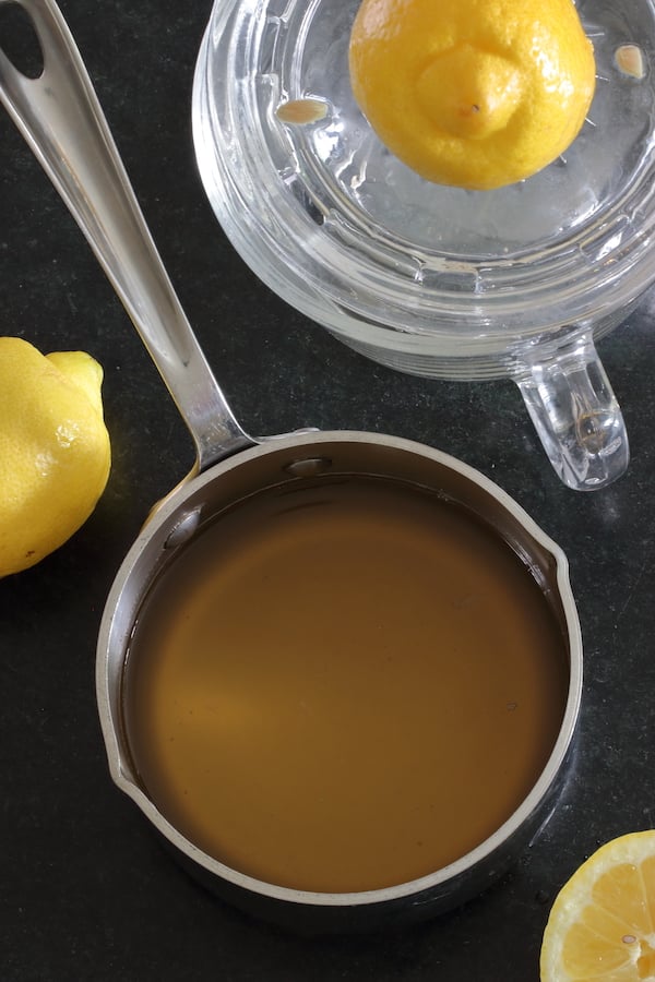 A small saucepan of simple syrup surrounded by lemons
