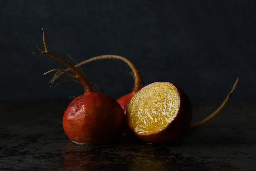 A whole golden beet and another cut in half artistically arranged on a black background.
