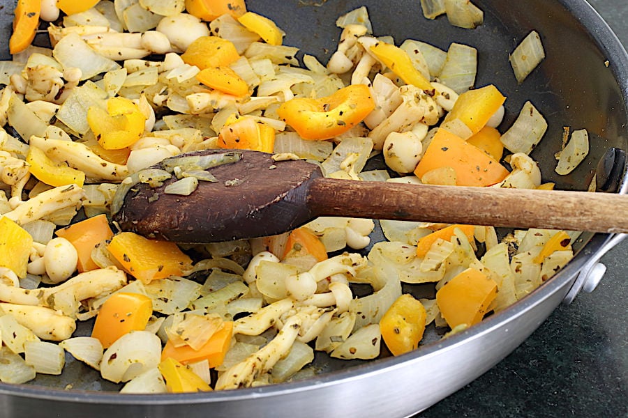 Broth sauteed onions, mushroom, peppers in a skillet being stirred with a wooden spoon