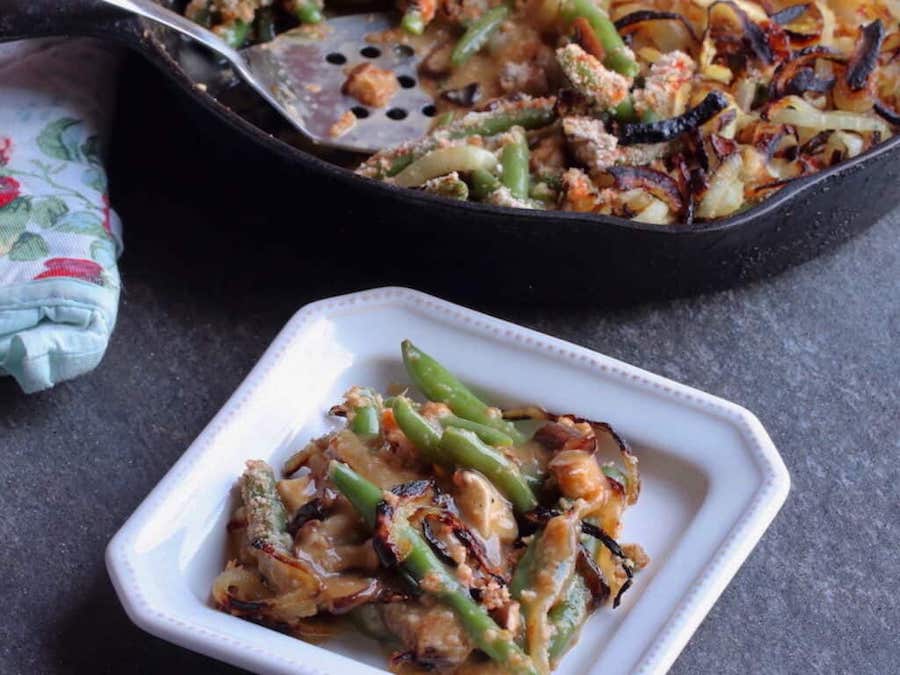 Green bean casserole in skillet with serving spatula and small dish of casserole in foreground