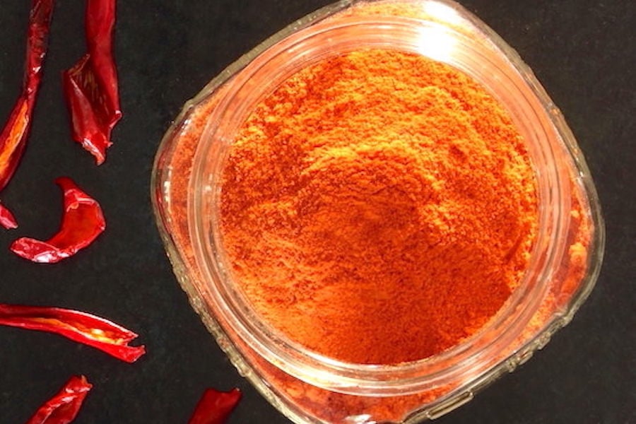 Ground paprika in a jar with dried peppers strewn about