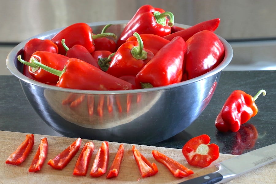A bowl of paprika peppers in the background and pepper strips cut in the foreground