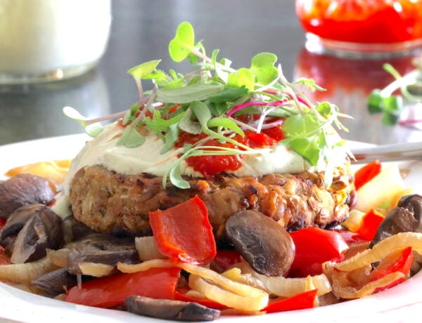 Vegan burger served over mushrooms, onion, and peppers; slathered in creamy dressing with a garnish of sprouts