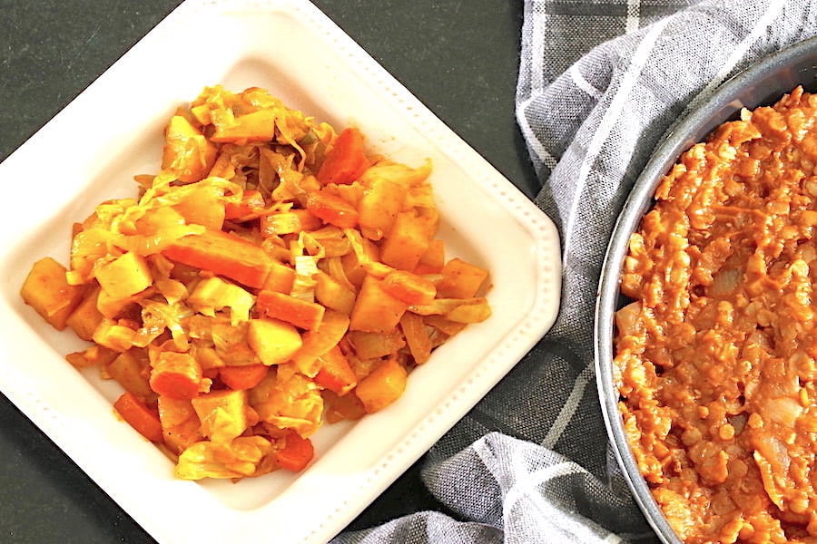 Ethiopian cabbage and potato stew served on a small square plate, with glimpse of spicy red lentils in a pan