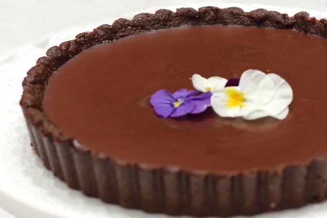 Close up chocolate tart with fresh flowers arranged on top