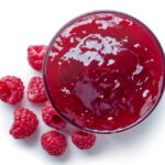 Raspberry Jam in jar with fresh raspberries strewn about