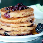 Stack of Fluffy Blueberry Oatmeal Pancakes with fresh wild blueberries on top, garnished with fresh blackberries and maple syrup