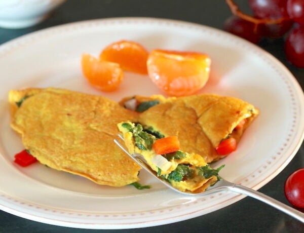 Forkful of Vegan Omelette highlighted with rest of omelette, mandarin orange sections, and grapes in background