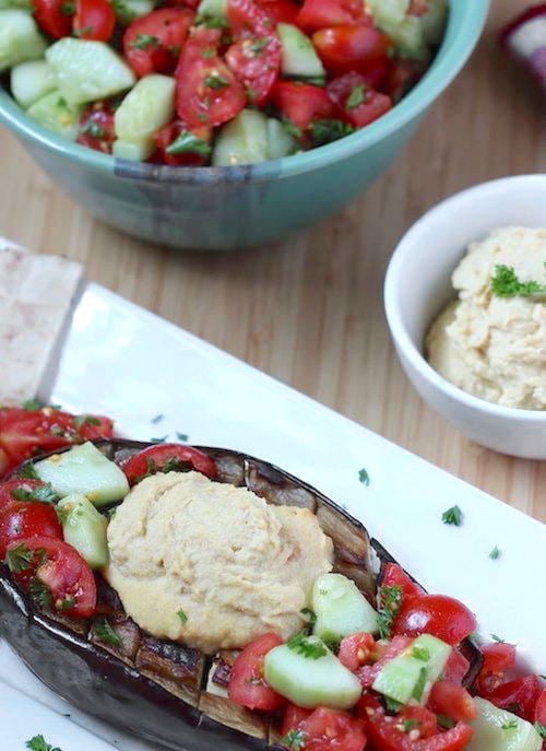 Sabich Boats on a plate with a small bowl of homemade hummus; Israeli salad in a bowl in the rear