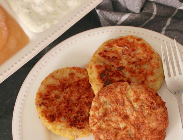 Three Vegan Potato Pancakes with Leeks plated; apple sauce and tzatziki sauce in the background and a checkered napkin to the side