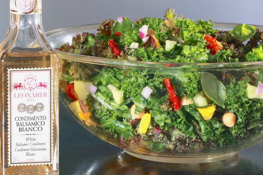 Kale and Chickpea Salad in a large clear glass bowl with a bottle of white balsamic vinegar to the side