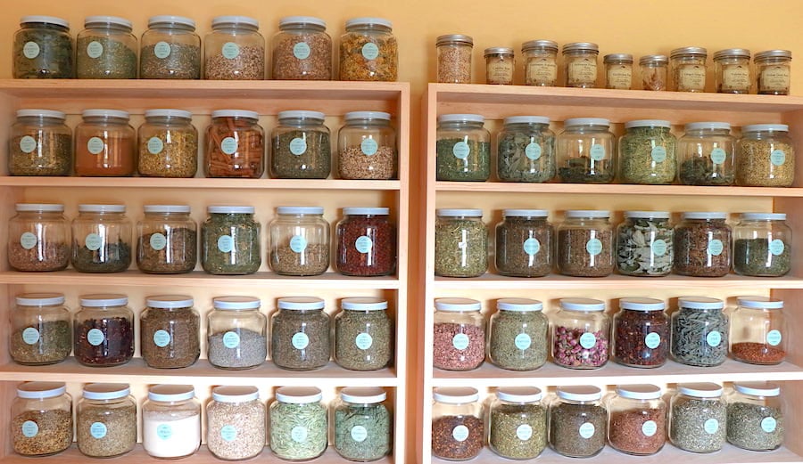 Over 50 half gallon jars filled with dry herbs arranged on pine shelving