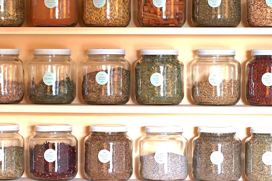 Close up of several half gallon jars filled with dry herbs and arranged on shelves