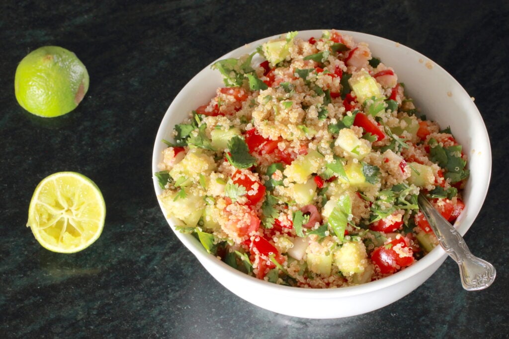 Zesty Quinoa Salad in a white bowl with spoon; halved lemon to the side