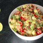 Zesty Quinoa Salad in a white bowl with spoon; halved lemon to the side