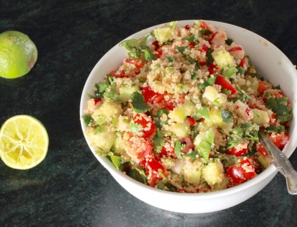 Zesty Quinoa Salad in a white bowl with spoon; halved lemon to the side