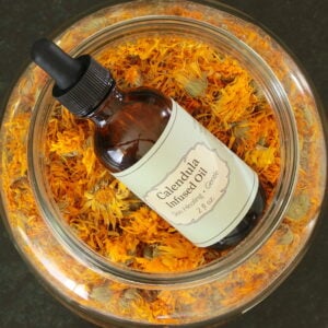 Bottle of calendula infused oil resting on top of jar of dried calendula blossoms